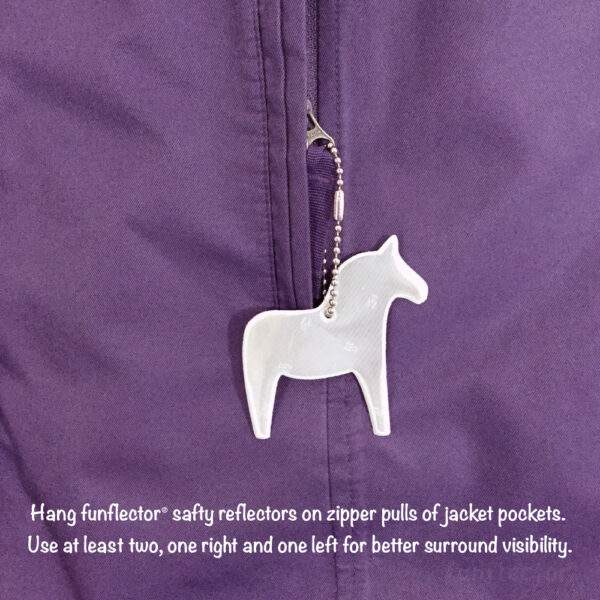 White dala horse safety reflector by funflector. Hanging on jacket pocket zipper pull.