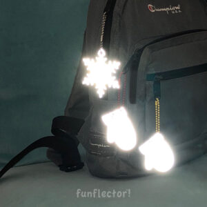 White snowflake and colorful mitten safety reflectors on backpack at night