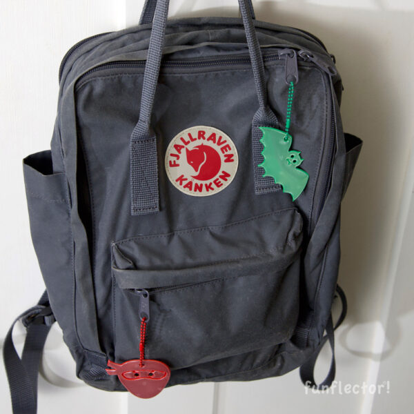 Green bat and red ninja safety reflector on backpack Kanken