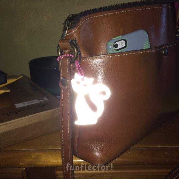 Pink cat safety reflector on brown purse at night